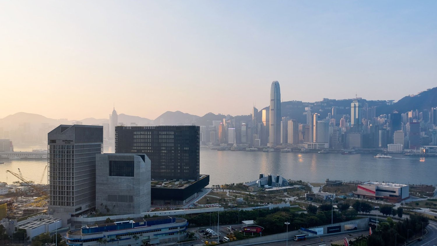 Cityscape of Hong Kong with tall skyscrapers, a harbour and mountains during daytime.